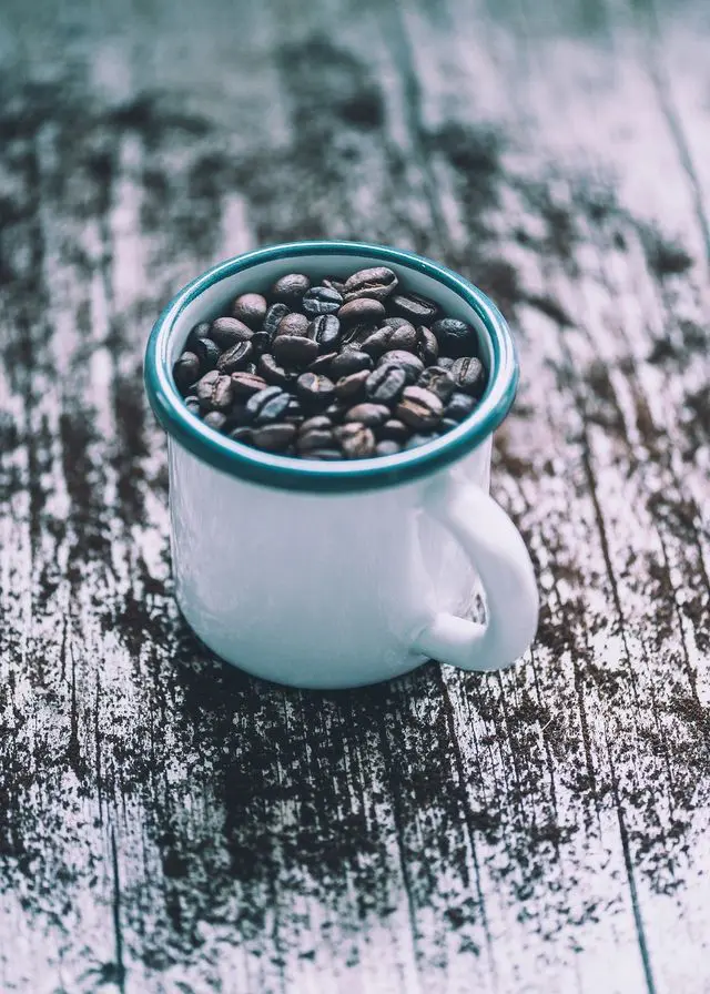 A cup of coffee beans on top of a wooden table.